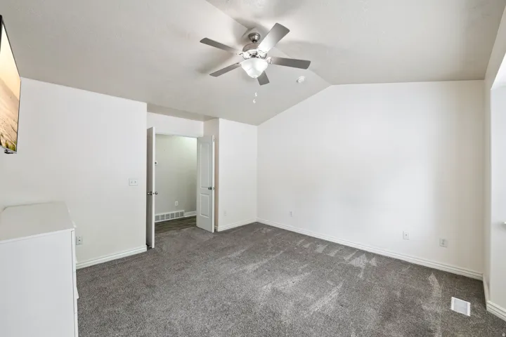Vaulted ceiling, ceiling fan with integrated lighting, gray carpeting, white walls, and white trim