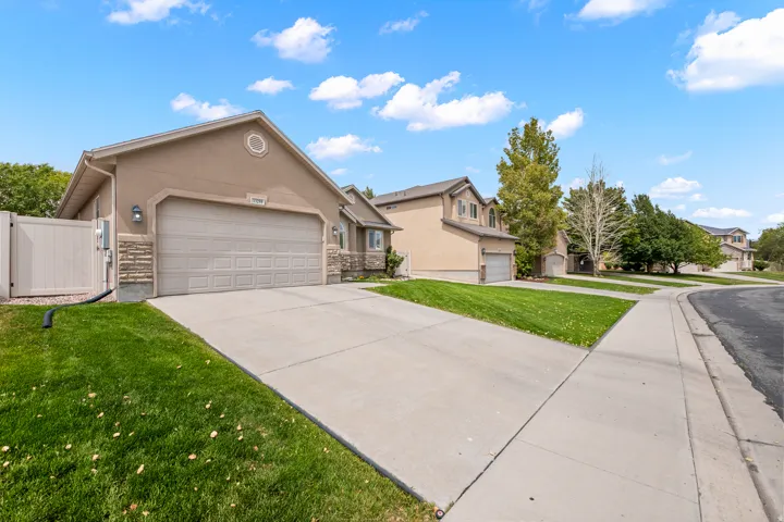 Stucco exterior with stone accents, attached two-car garage, concrete driveway, and mature landscaping