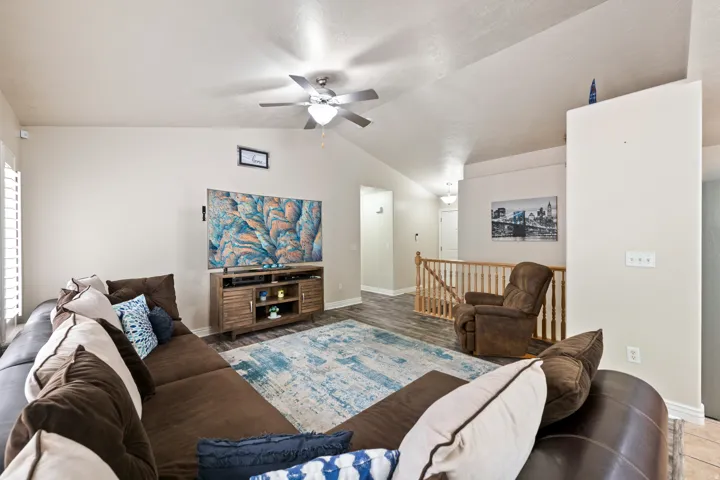 Spacious living area featuring vaulted ceilings, wood-finish flooring, plantation shutters, and a ceiling fan