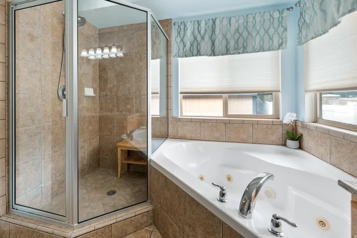 Walk-in shower with clear glass enclosure, corner soaking tub with deck-mounted fixtures, and tiled surround