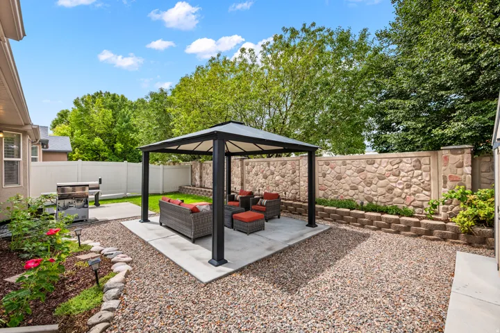 Expansive backyard featuring a stone-clad privacy wall, a covered gazebo on a concrete pad, a manicured lawn area, and gravel landscaping