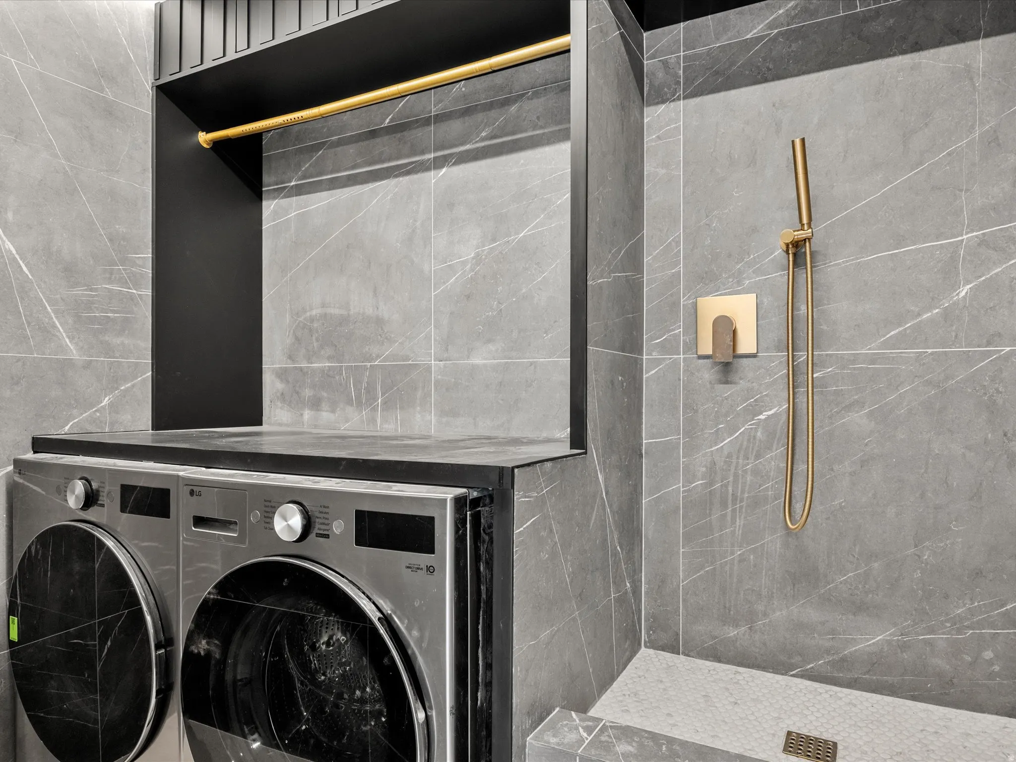 Integrated laundry area with washer/dryer and dog bath, featuring a gold-toned hanging rod, a dark countertop, and large format wall tile