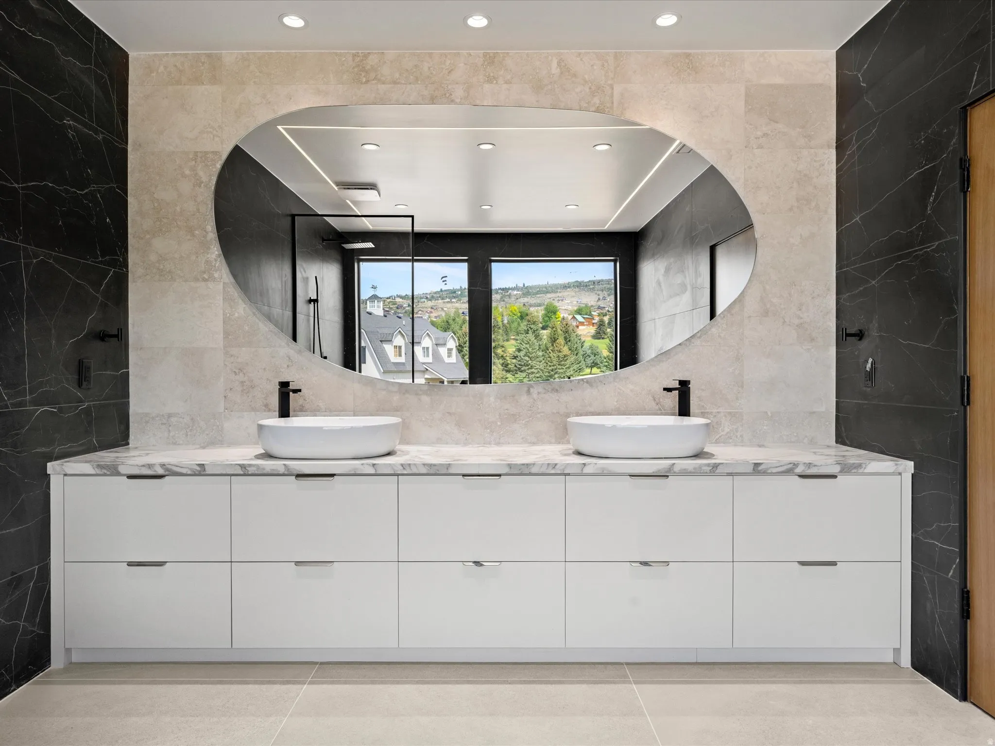 2nd Level Master En-Suite, Dual vessel sinks with matte black faucets, integrated white cabinetry, stone-finish countertops, and an oval mirror