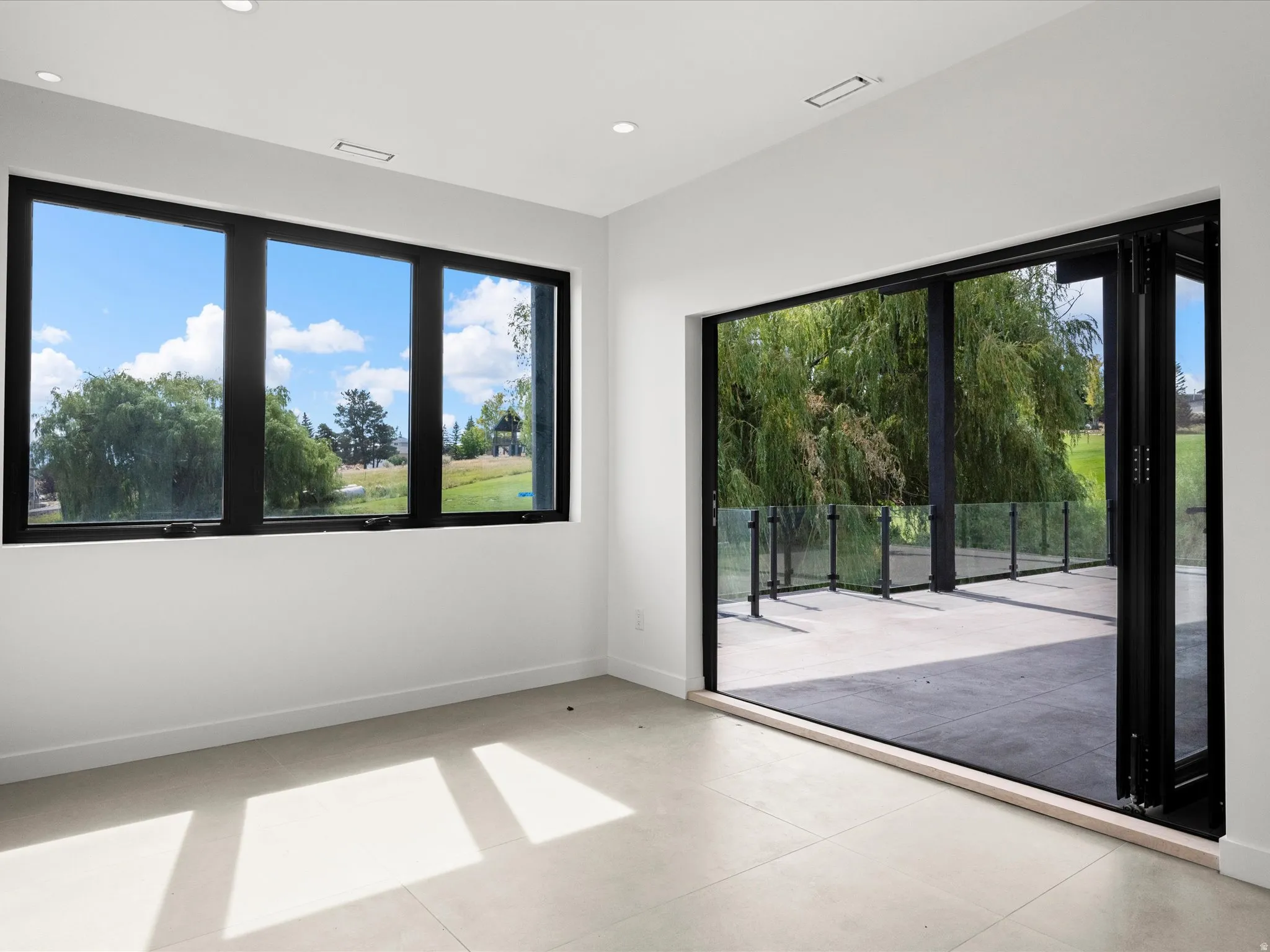 Expansive multi-panel windows, large folding glass door, recessed ceiling lighting, light-toned flooring, and a spacious outdoor patio with glass railing