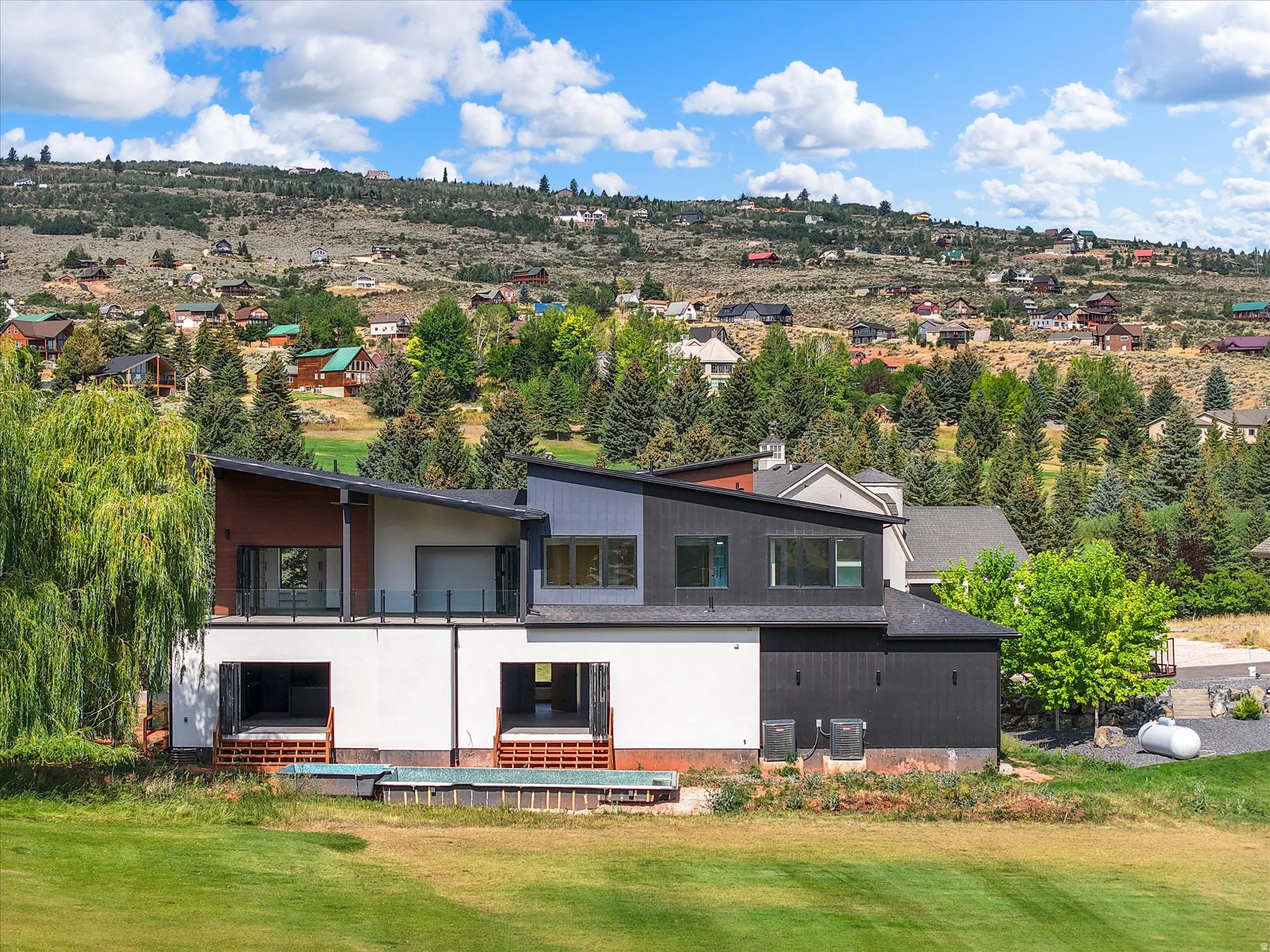 Modern architectural design featuring multi-level construction, multiple balconies with glass railings, an integrated plunge pool, and expansive green space