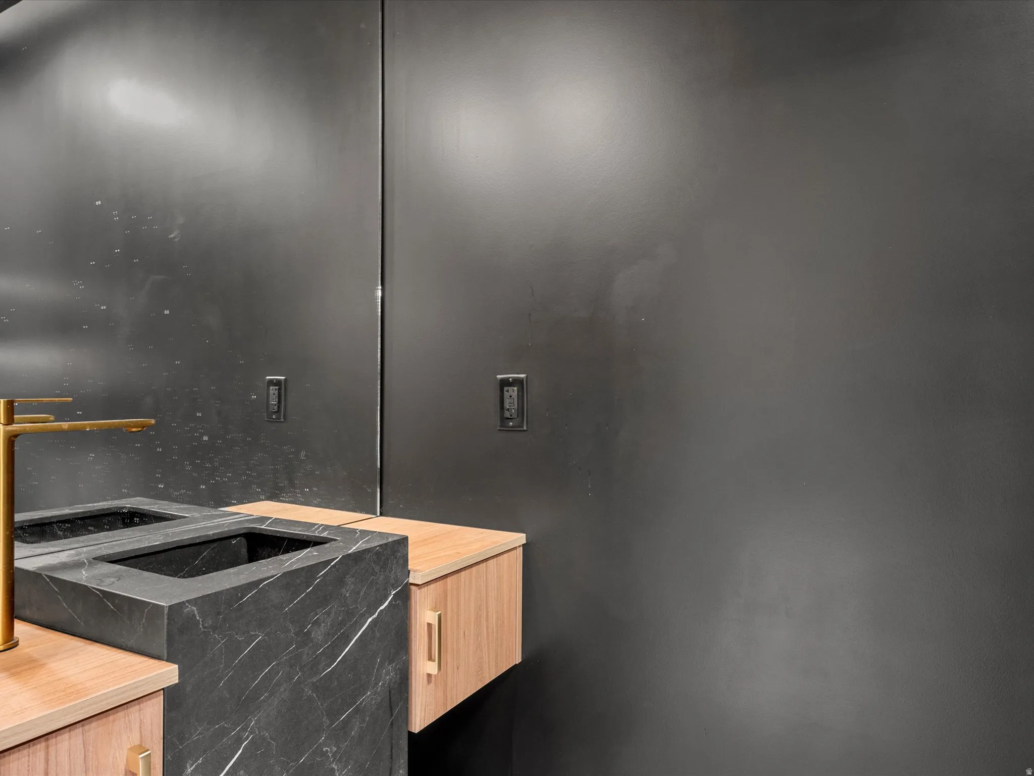 Floating wood-finish vanity with gold hardware, integrated dark stone sink, and wall-mounted gold-finish faucet