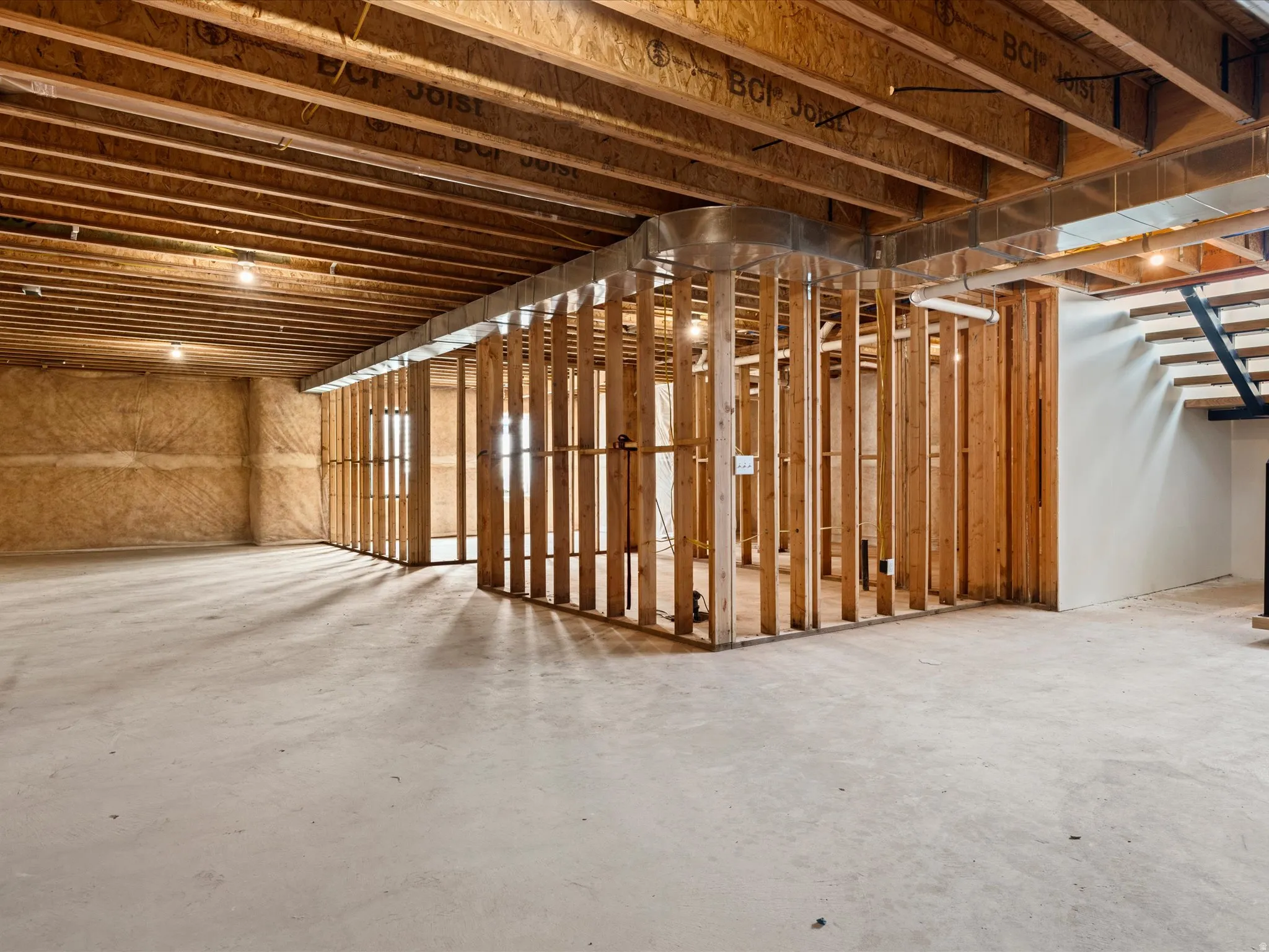 Unfinished basement with concrete flooring, exposed wood joists, and structural wood framing