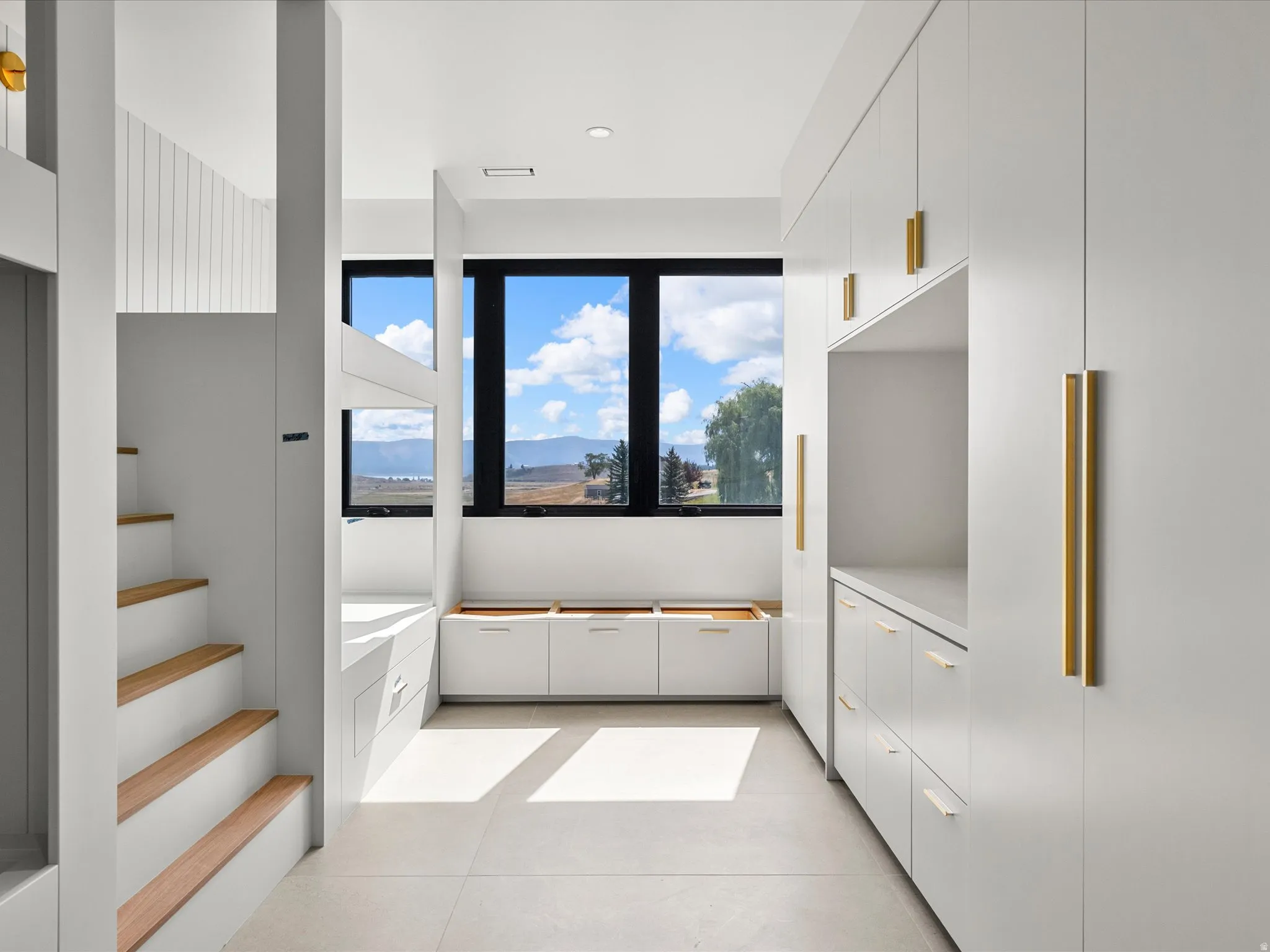 Built-in cabinetry with gold-toned hardware, light wood-finish stairs, and expansive windows