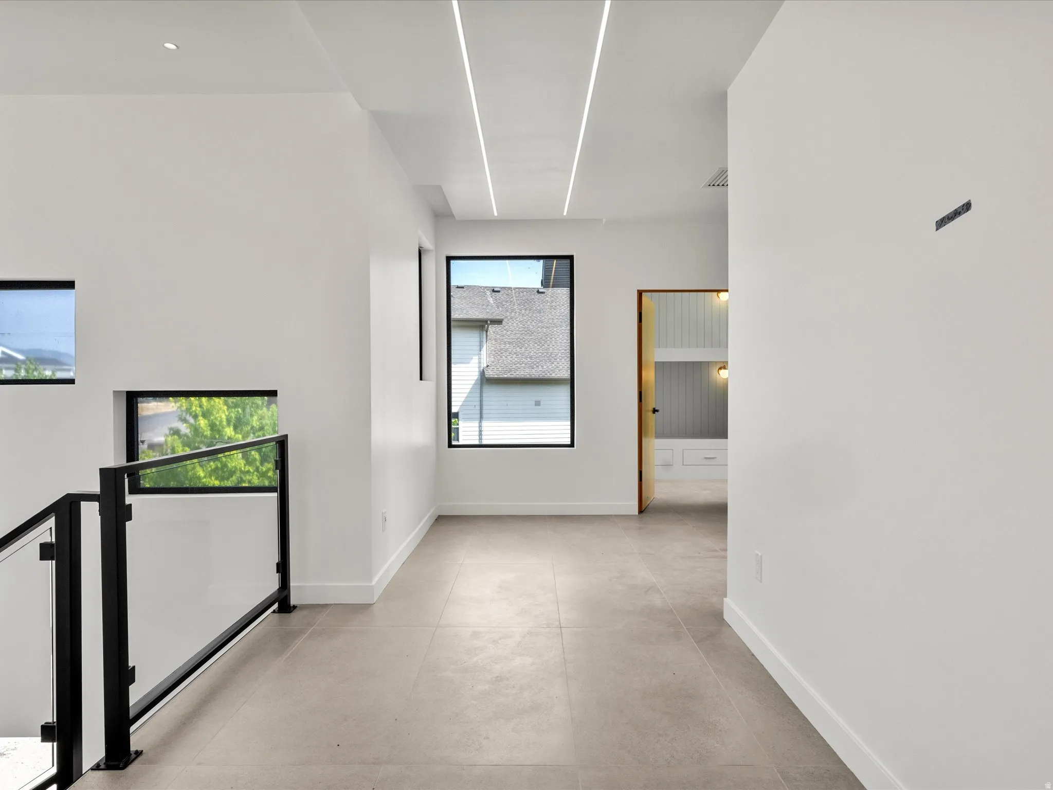 Recessed linear lighting, tile flooring, black frame windows, and a glass panel railing