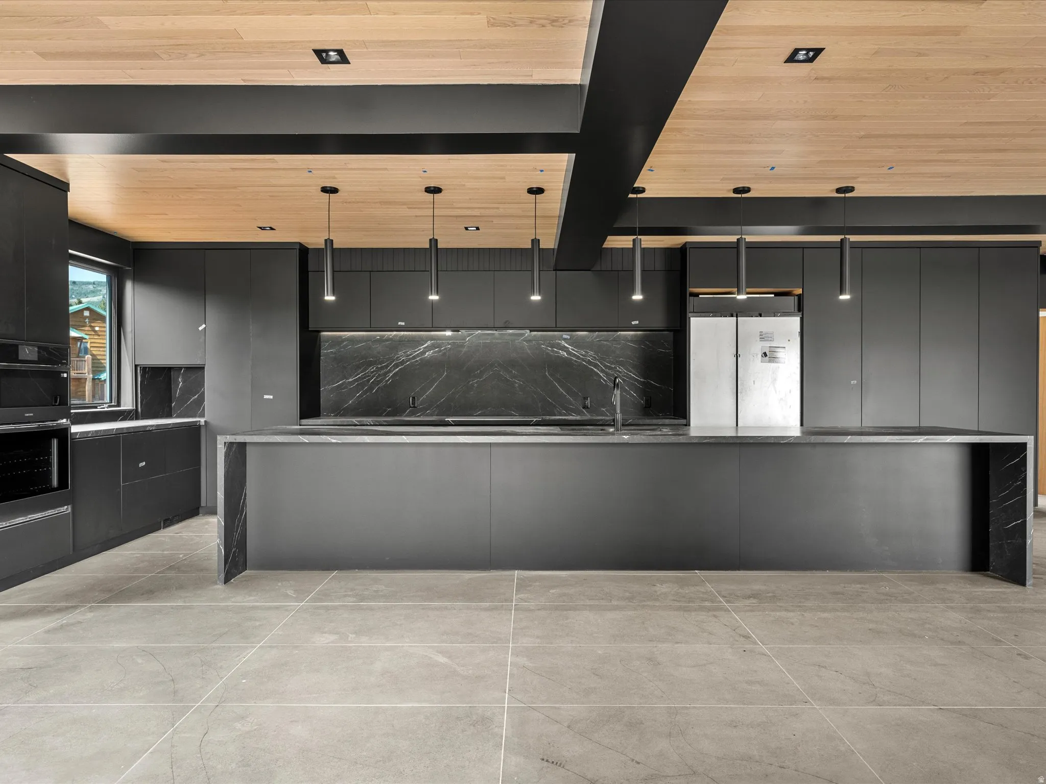 Contemporary kitchen featuring dark flat-panel cabinetry, a large center island, black marble-look countertops and backsplash, integrated stainless steel appliances, and wood-finish ceiling panels