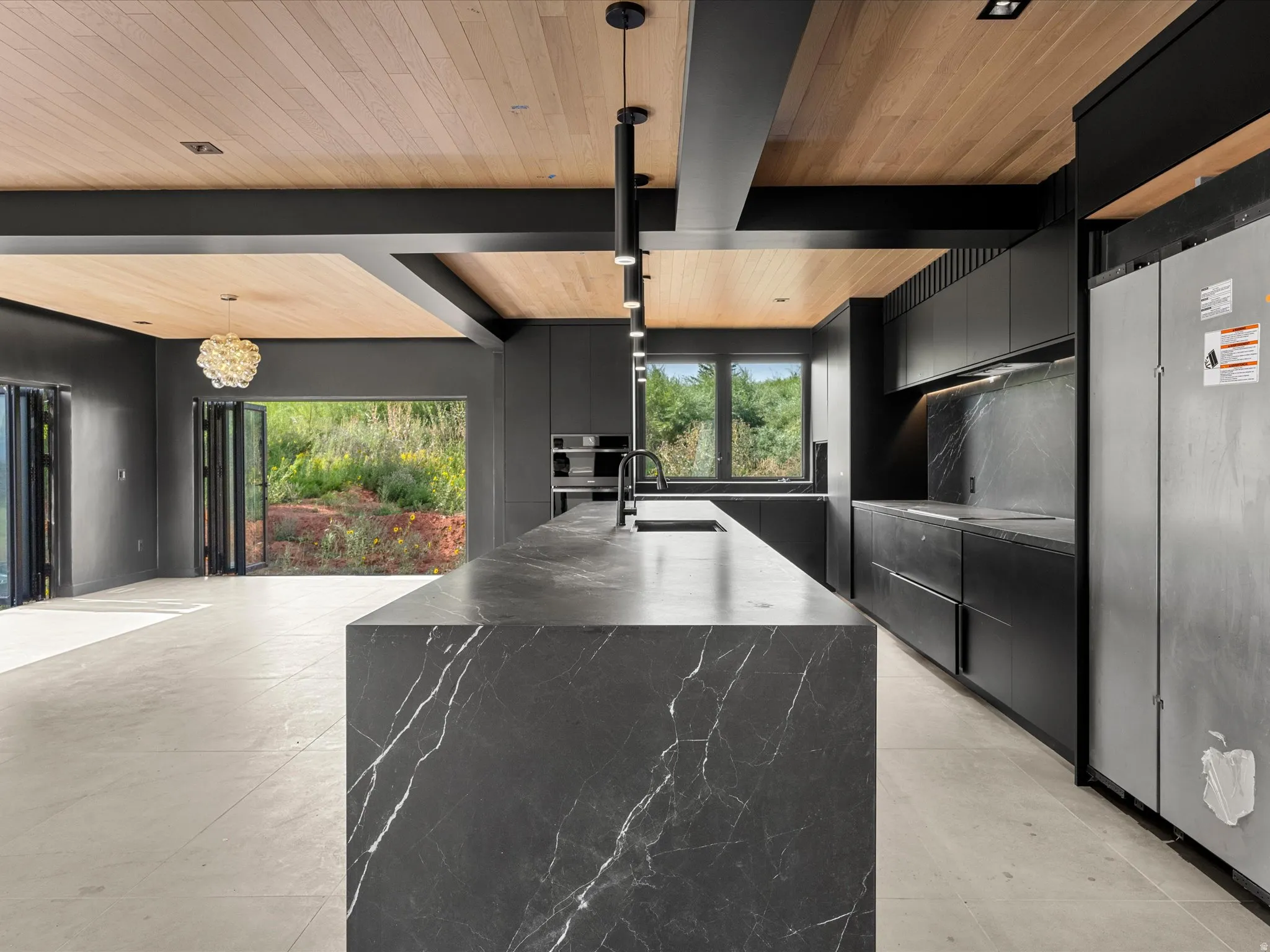 Kitchen featuring a waterfall island with a dark stone finish, integrated appliances, wood-finish ceiling, bi-fold doors, and recessed and pendant lighting