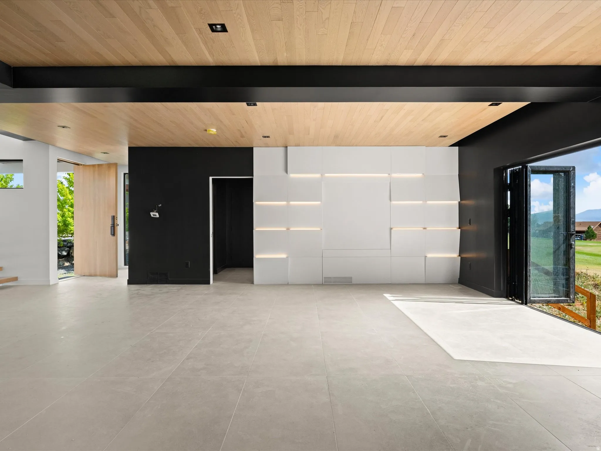 Light wood-finish ceiling, large format tile flooring, black accent wall, built-in wall feature with integrated lighting, and multi-panel folding glass doors