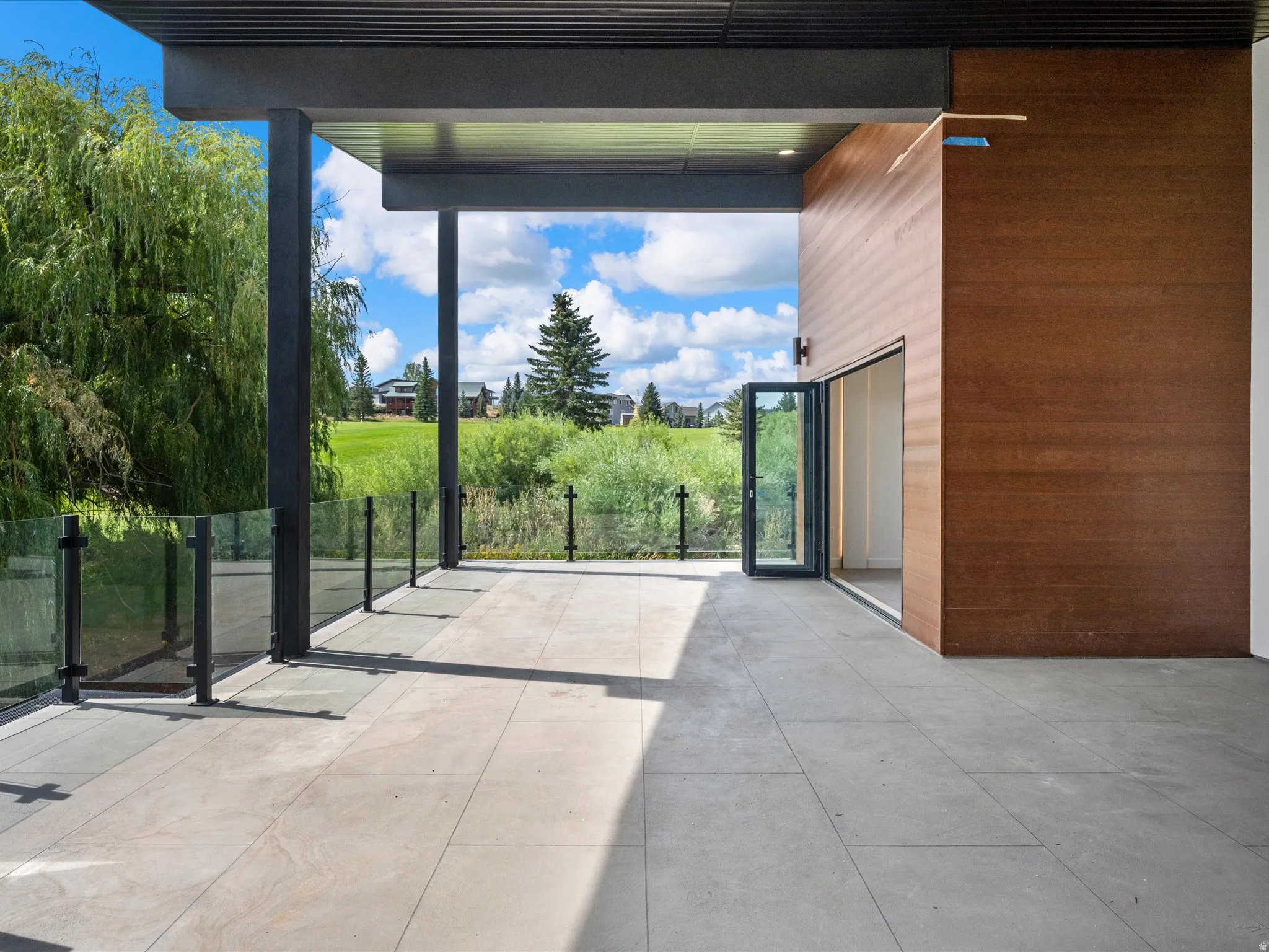 Expansive outdoor patio with large format tile flooring, glass panel railing, and wood-paneled exterior wall