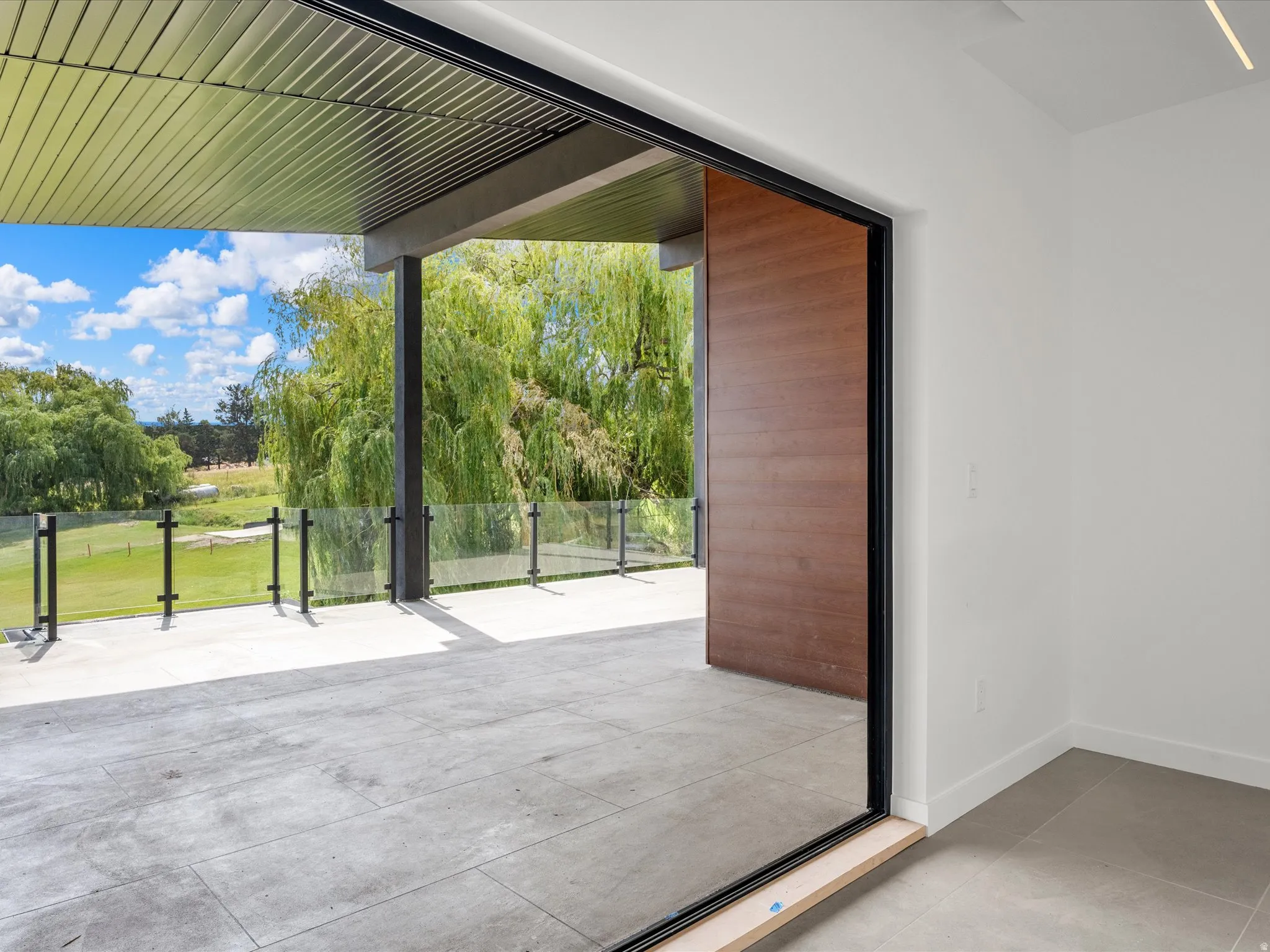 Spacious outdoor balcony with a glass railing system and a wood-panel accent wall