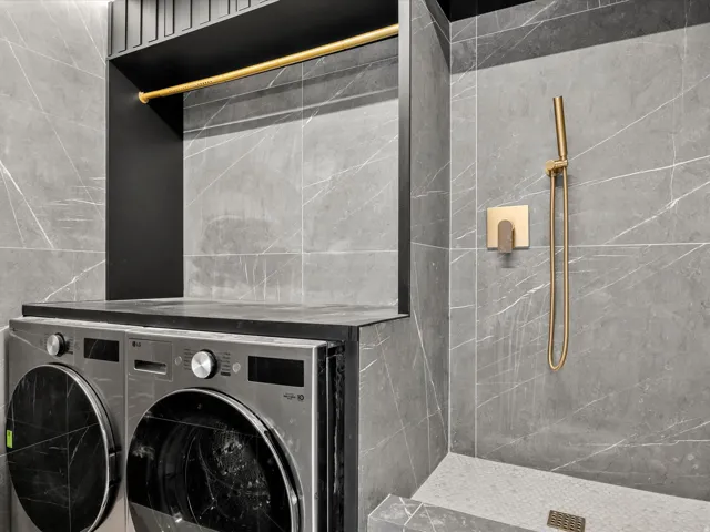 Integrated laundry area with washer/dryer and dog bath, featuring a gold-toned hanging rod, a dark countertop, and large format wall tile