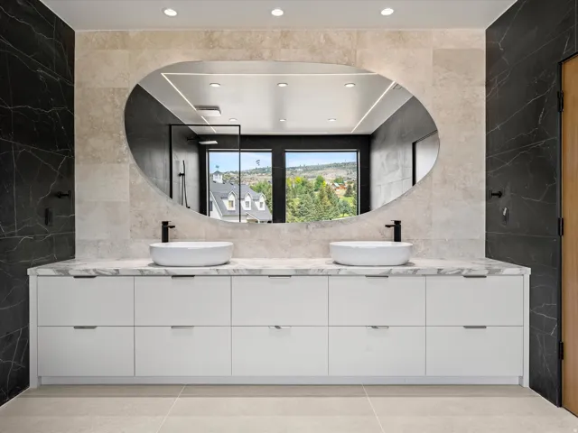 2nd Level Master En-Suite, Dual vessel sinks with matte black faucets, integrated white cabinetry, stone-finish countertops, and an oval mirror