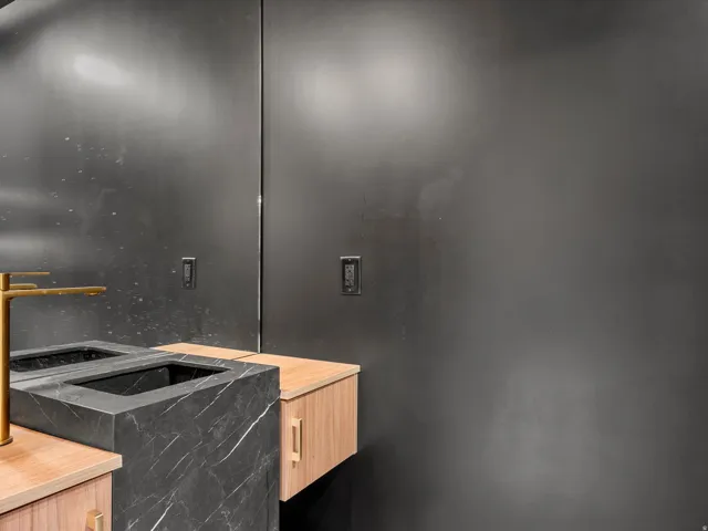 Floating wood-finish vanity with gold hardware, integrated dark stone sink, and wall-mounted gold-finish faucet