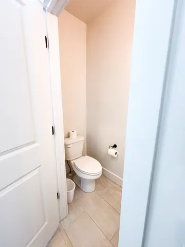 White panel door, light-toned wall paint, ceramic tile flooring, and white toilet fixture