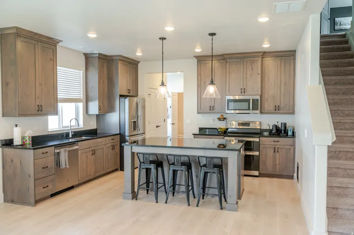 Kitchen featuring wood-finish cabinetry, stainless steel appliances, dark countertops, a central island with seating, and recessed lighting
