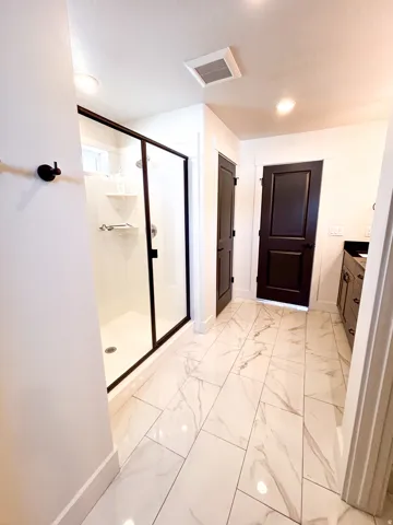 Spacious bathroom featuring large format tile flooring, a walk-in shower with a glass enclosure, a dark wood-finish vanity, and recessed lighting