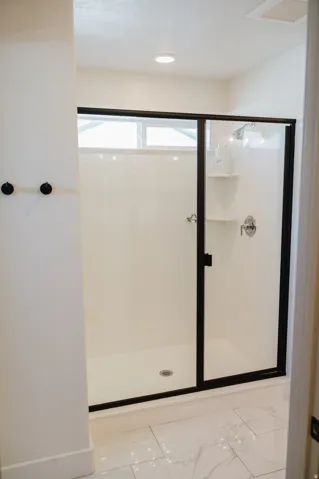 Spacious shower with a frameless glass enclosure, matte black trim, built-in shelving, and a transom window