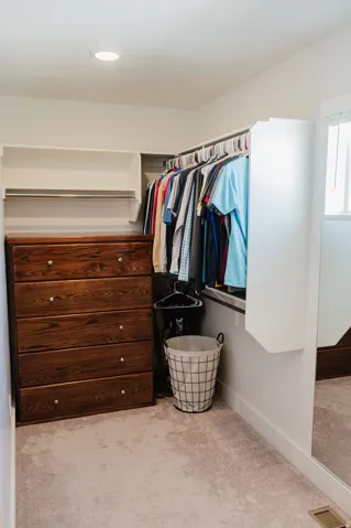 Recessed ceiling light, built-in shelving, hanging clothes rods, built-in wood-finish dresser with drawer pulls, and carpeted flooring