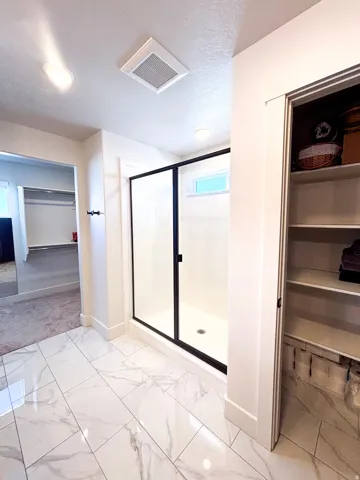 Walk-in shower with black-framed glass enclosure, white tile flooring, recessed lighting, and built-in shelving