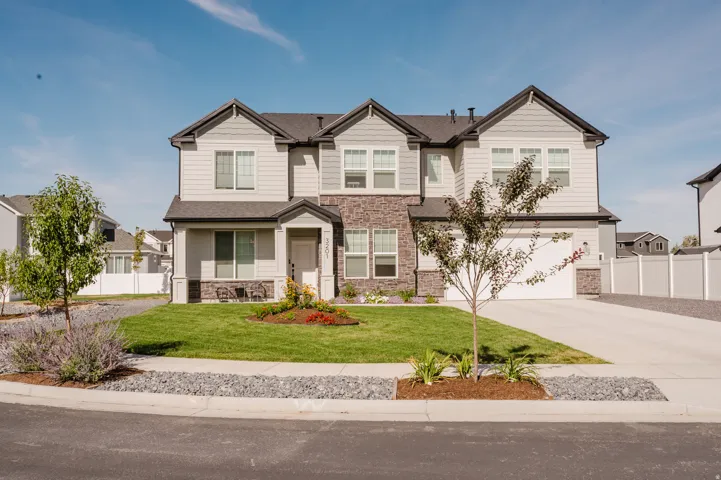 Contemporary two-story residence with stone and siding exterior, front lawn, established landscaping, and attached garage