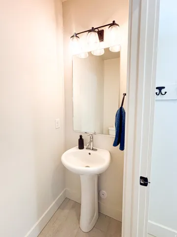 Pedestal sink with chrome faucet, framed mirror, and a three-light vanity fixture