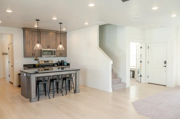 Kitchen island with seating, stainless steel microwave, wood-finish cabinetry, light wood-finish flooring, and recessed lighting
