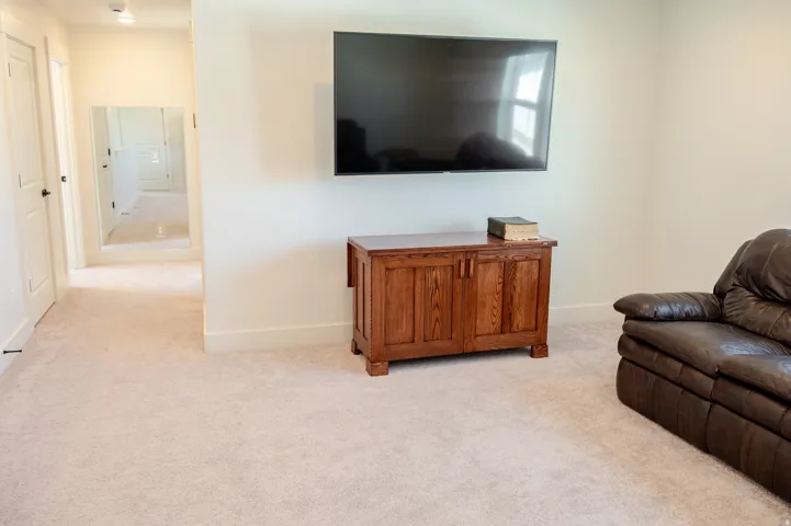 Wall-mounted television with a dedicated entertainment console, light-colored carpeting, and a recessed ceiling light