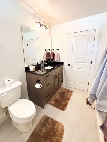 Vanity with dark wood-finish cabinetry, black countertop, rectangular undermount sink, and contemporary vanity light fixture