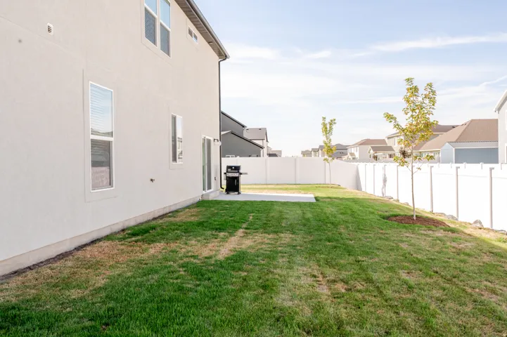 Expansive lawn with a concrete patio, white vinyl fencing, and young trees