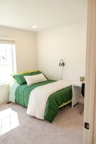 Plush carpet flooring, recessed ceiling lighting, and a window with a roller shade