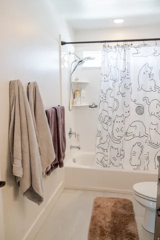 White bathtub with an integrated shower, featuring a window and wall-mounted shelving