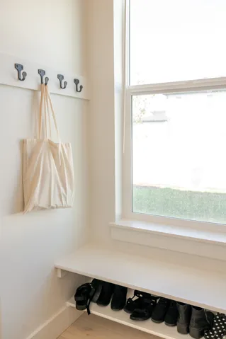 Built-in bench with shoe storage, window, wall-mounted coat rack with five hooks, and wood-finish flooring