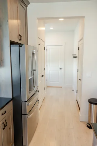 Stainless steel refrigerator, light wood-finish flooring, recessed lighting, white interior doors with dark hardware, and light-toned cabinetry