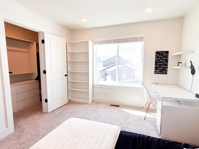 Recessed lighting, soft carpet flooring, built-in shelving, large window with blinds, and an organized closet with built-in drawers