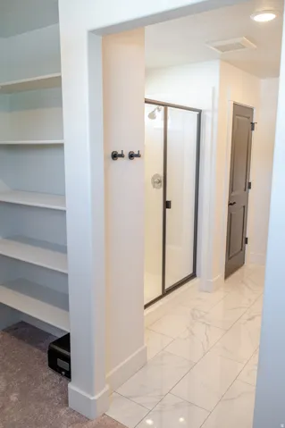 Built-in shelving, glass-enclosed shower with black trim, black interior door, recessed lighting, and large format tile flooring