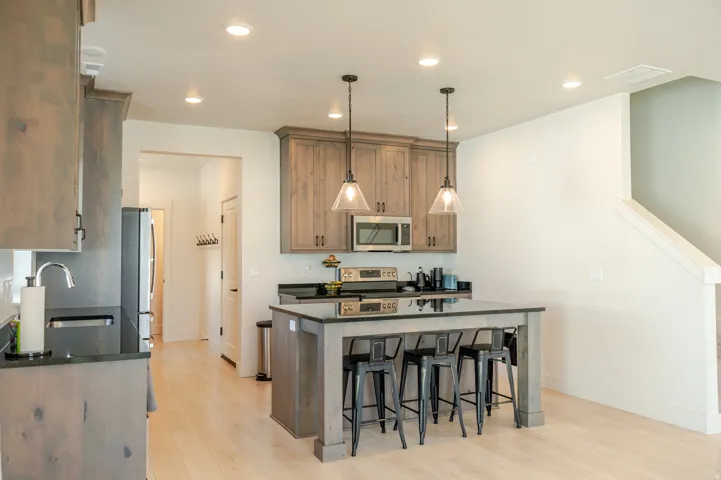 Kitchen featuring wood-finish cabinetry, black countertops, a stainless steel microwave, and an island with pendant lighting