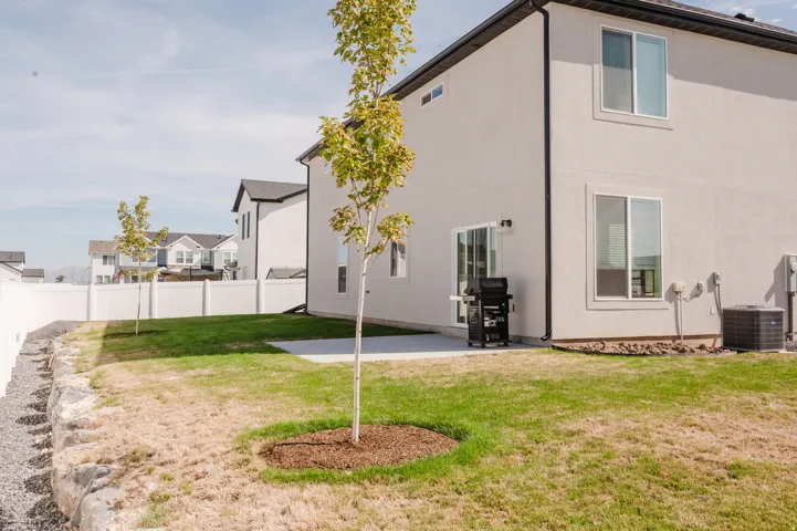 Rear exterior featuring light-colored stucco, white vinyl fencing, a concrete patio, and a well-maintained lawn