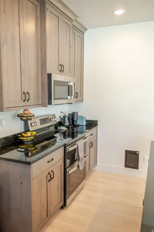 Wood-finish cabinetry with dark hardware, dark countertops, stainless steel range with double oven, and stainless steel microwave