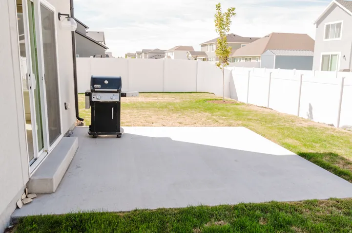 Expansive concrete patio with direct access to a large lawn, bordered by a white privacy fence