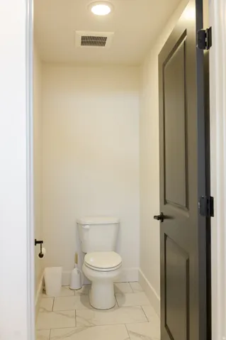 Recessed ceiling light, white tile flooring, white wall paint, dark paneled door, white toilet