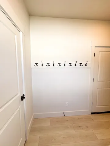 Light wood-finish flooring, white paneled doors, and wall-mounted coat hooks