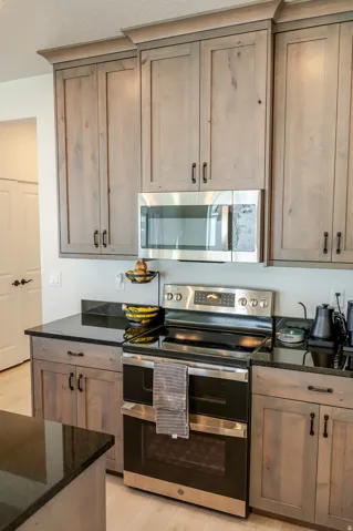 Integrated stainless steel microwave, black electric range with a double oven, wood-finish cabinetry, and black countertops
