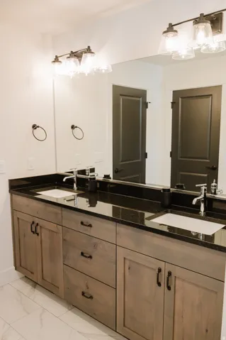 Double vanity with wood-finish cabinetry, black countertops, and undermount sinks