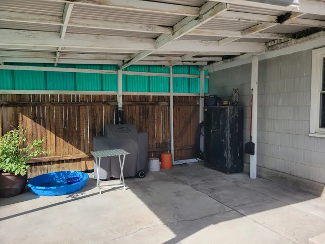 Covered patio with concrete flooring, wood privacy fencing, and a corrugated roof