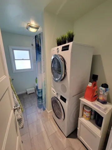 Tiled flooring, stacked laundry appliances, and a window