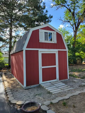 Red gambrel shed with white trim, featuring a window with decorative shutters